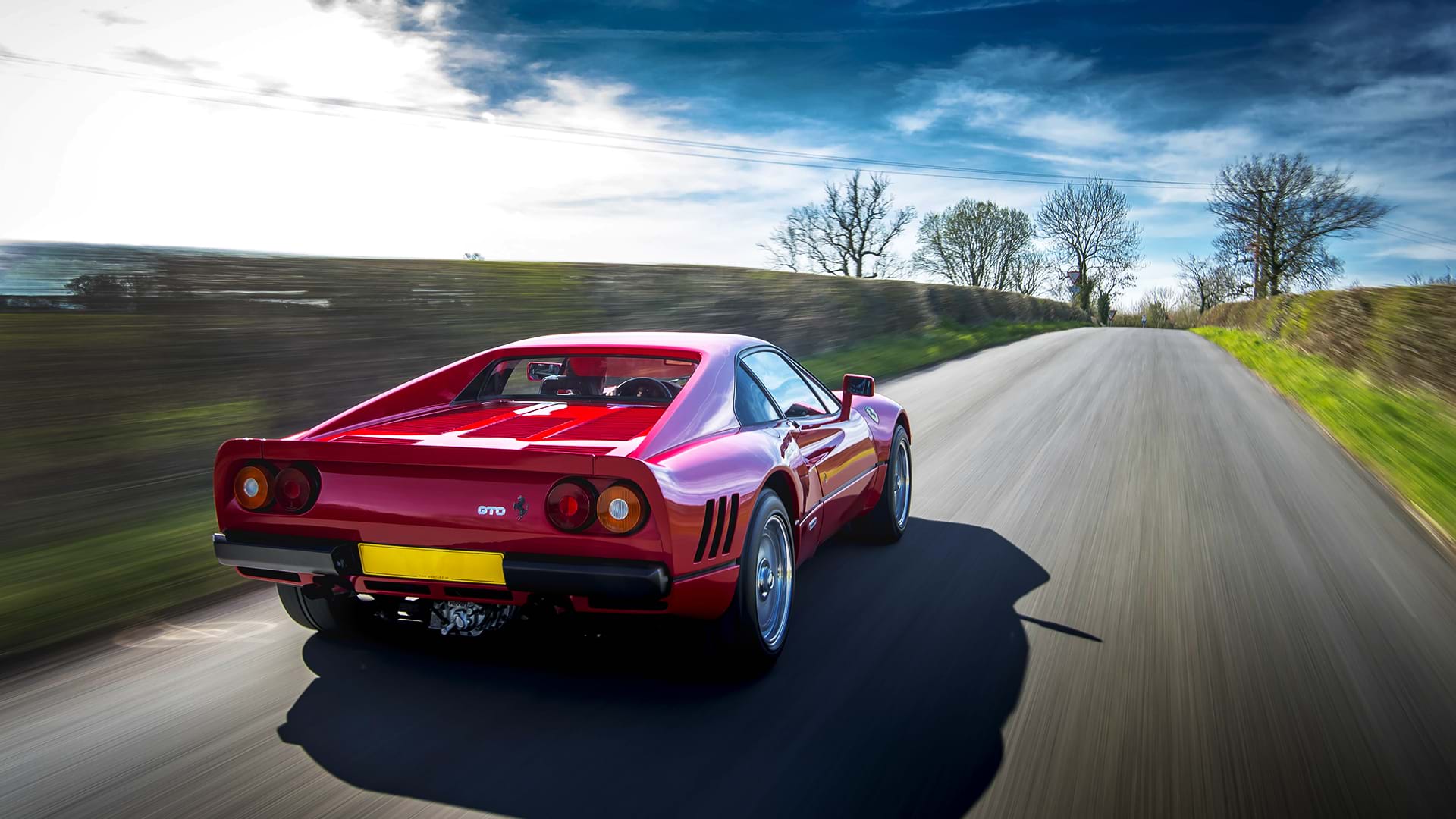 Clásico rojo Ferrari 288 GTO acelerando por una pintoresca carretera rural. 