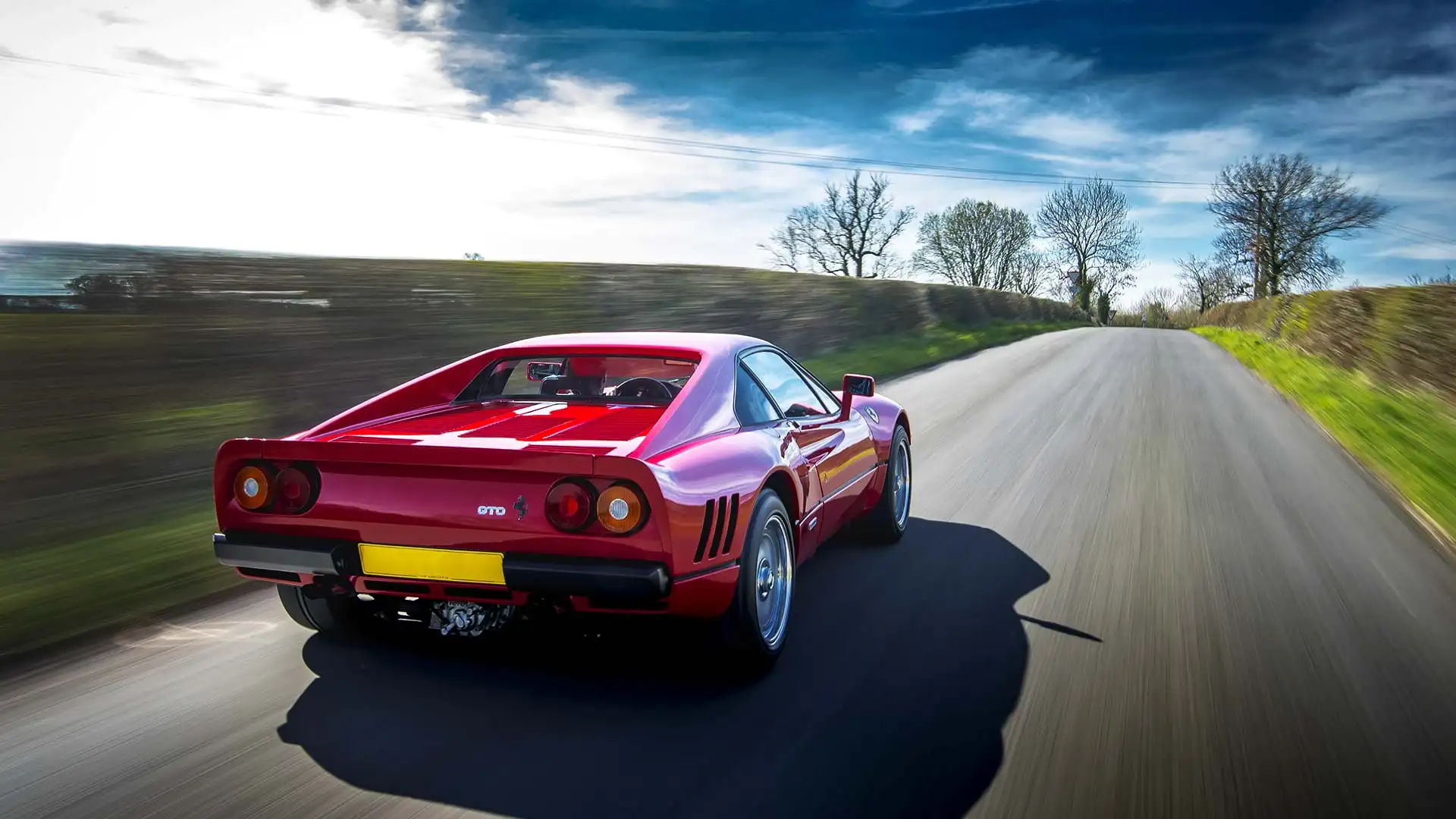 Clásico rojo Ferrari 288 GTO acelerando por una pintoresca carretera rural. 
