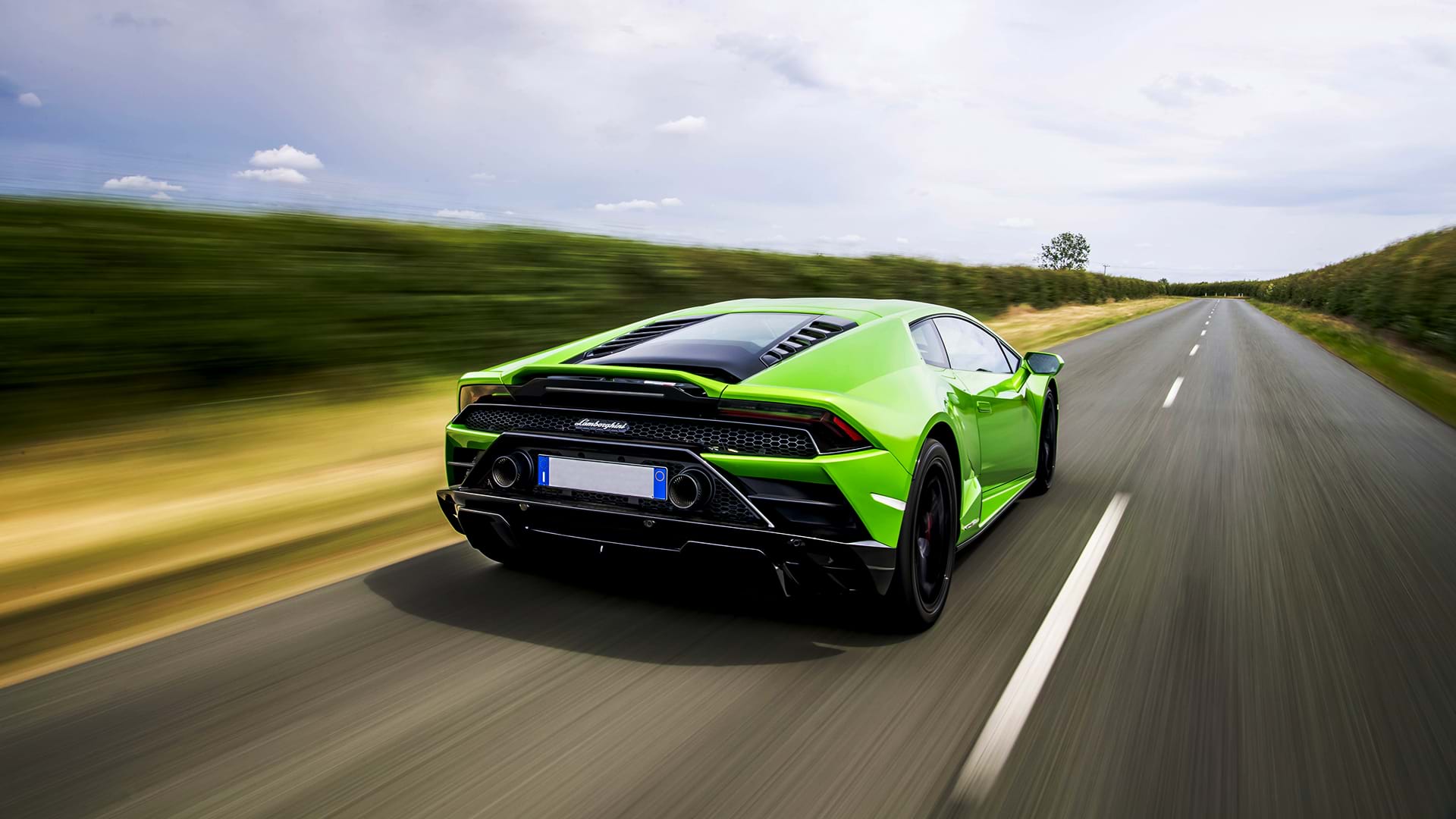 Verde brillante Lamborghini Huracán Evo acelerando por un camino rural en un día soleado.