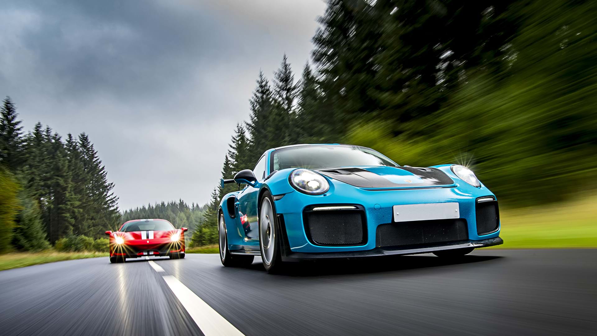 RS azul Porsche ​​991 GT3 que conduce a una pista roja Ferrari 488 en una carretera panorámica. 