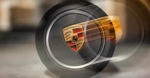 Airbag en el volante de Porsche con el escudo detallado de Porsche en un efecto de desenfoque de movimiento de primer plano.